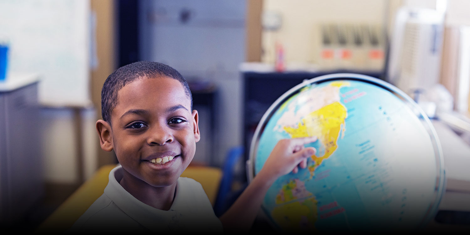 Smiling student pointing to a place on a globe.